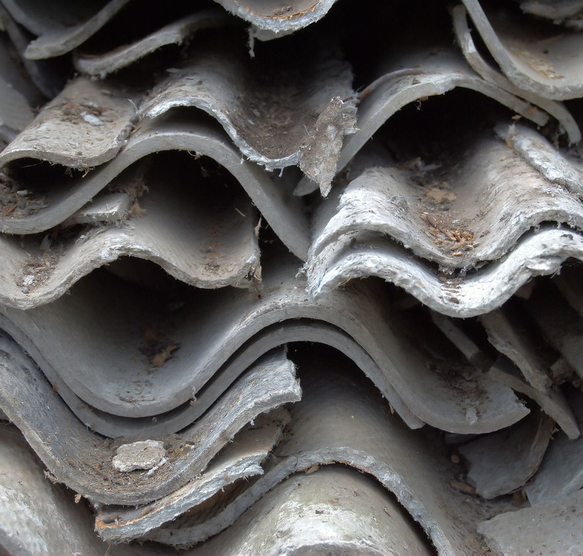 Nahaufnahme von gestapelten Asbestzementplatten mit sichtbaren Alterungs- und Abnutzungserscheinungen.
